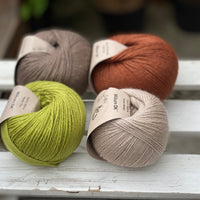 Four balls of yarn in two rows of two. There is a beige ball, a brown ball, a reddish-brown ball and a green ball.