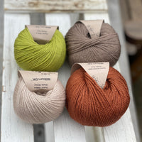 Four balls of yarn in two rows of two. There is a beige ball, a brown ball, a reddish-brown ball and a green ball.