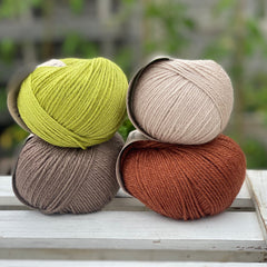Four balls of yarn in two rows of two. There is a beige ball, a brown ball, a reddish-brown ball and a green ball.