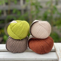 Four balls of yarn in two rows of two. There is a beige ball, a brown ball, a reddish-brown ball and a green ball.