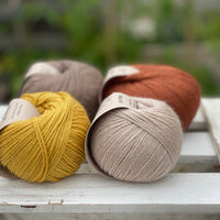 Four balls of yarn in two rows of two. There is a beige ball, a brown ball, a reddish-brown ball and a yellow ball.
