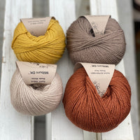 Four balls of yarn in two rows of two. There is a beige ball, a brown ball, a reddish-brown ball and a yellow ball.