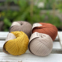 Four balls of yarn in two rows of two. There is a beige ball, a brown ball, a reddish-brown ball and a yellow ball.