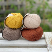 Four balls of yarn in two rows of two. There is a beige ball, a brown ball, a reddish-brown ball and a yellow ball.
