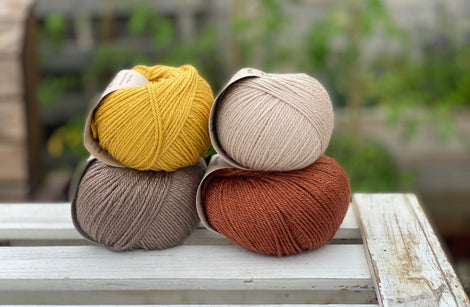 Four balls of yarn in two rows of two. There is a beige ball, a brown ball, a reddish-brown ball and a yellow ball.