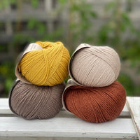 Four balls of yarn in two rows of two. There is a beige ball, a brown ball, a reddish-brown ball and a yellow ball.