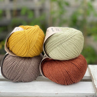 Four balls of yarn in two rows of two balls. There is a yellow ball, a brown ball, a pale green ball and a reddish brown ball.