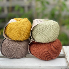 Four balls of yarn in two rows of two balls. There is a yellow ball, a brown ball, a pale green ball and a reddish brown ball.
