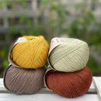 Four balls of yarn in two rows of two balls. There is a yellow ball, a brown ball, a pale green ball and a reddish brown ball.