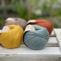 Four balls of yarn in two rows of two balls. There is a yellow ball, a brown ball, a blue-green ball and a reddish brown ball.