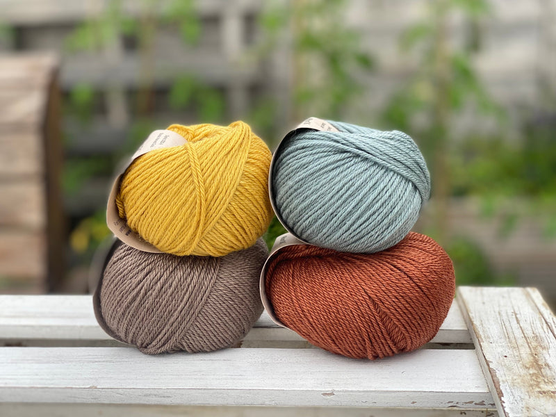 Four balls of yarn in two rows of two balls. There is a yellow ball, a brown ball, a blue-green ball and a reddish brown ball.