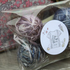 A clear plastic bag filled with small balls of yarn in shades of purple, blue and grey
