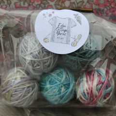 A clear plastic bag filled with small balls of yarn in shades of grey, green, blue and pink
