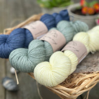 Three skeins of yarn. From left to right - a dark blue skein, a light blue-green skein and a pale yellow skein