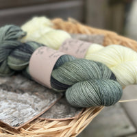 Two skeins of yarn - one variegated green skein and one pale yellow skein