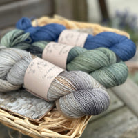 Three skeins of yarn. From left to right - a variegated grey and brown skein, a variegated green skein and a dark blue skein