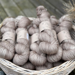 A white wicker basket containing several skeins of light brown yarn