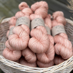 A white wicker basket containing several skeins of pink yarn