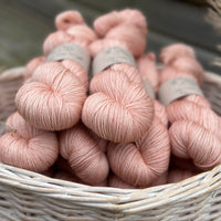 A white wicker basket containing several skeins of pink yarn