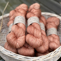 A white wicker basket containing several skeins of brownish pinky yarn