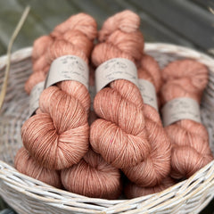 A white wicker basket containing several skeins of brownish pinky yarn