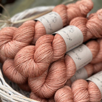 A white wicker basket containing several skeins of brownish pinky yarn