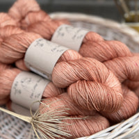 A white wicker basket containing several skeins of brownish pinky yarn