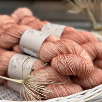 A white wicker basket containing several skeins of brownish pinky yarn