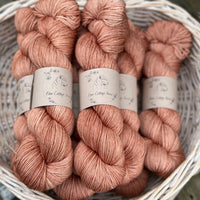 A white wicker basket containing several skeins of brownish pinky yarn