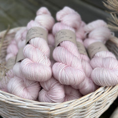 A white wicker basket containing several skeins of pale pink yarn