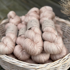 A white wicker basket containing several skeins of beige yarn