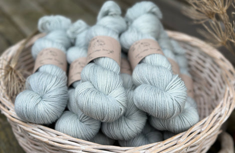 A white wicker basket containing several skeins of pale blue yarn