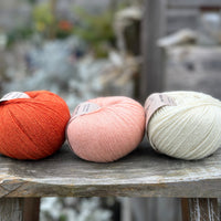 Three balls of yarn - from left to right an orange ball, a peachy orange ball and a cream ball