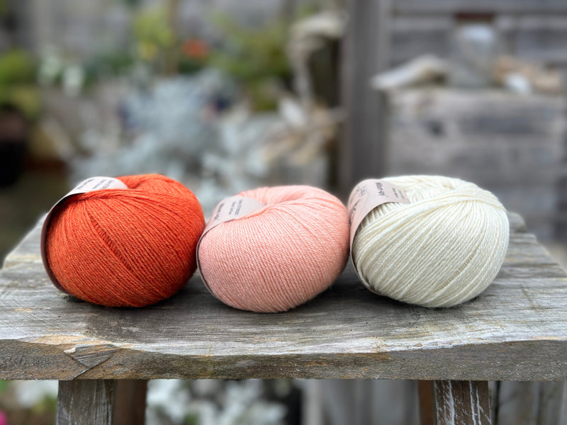 Three balls of yarn - from left to right an orange ball, a peachy orange ball and a cream ball