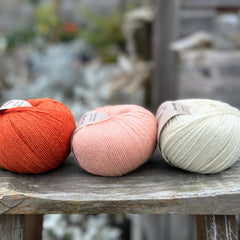 Three balls of yarn - from left to right an orange ball, a peachy orange ball and a cream ball