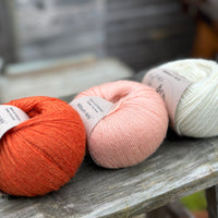 Three balls of yarn - from left to right an orange ball, a peachy orange ball and a cream ball