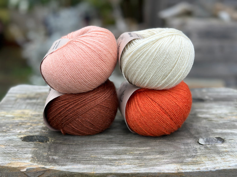 Four balls of yarn in two rows of two balls. The top row has a peachy orange ball and a cream ball. The bottom row has a reddish brown ball and an orange ball
