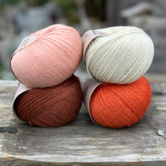 Four balls of yarn in two rows of two balls. The top row has a peachy orange ball and a cream ball. The bottom row has a reddish brown ball and an orange ball