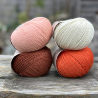 Four balls of yarn in two rows of two balls. The top row has a peachy orange ball and a cream ball. The bottom row has a reddish brown ball and an orange ball