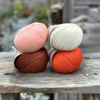 Four balls of yarn in two rows of two balls. The top row has a peachy orange ball and a cream ball. The bottom row has a reddish brown ball and an orange ball