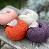 Four balls of yarn. From left to right there is a peachy pink ball, an orange ball, a cream ball and a dark purple ball.
