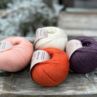 Four balls of yarn. From left to right there is a peachy pink ball, an orange ball, a cream ball and a dark purple ball.