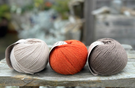 Three balls of yarn. From left to right: a beige ball, an orange ball and a brown ball