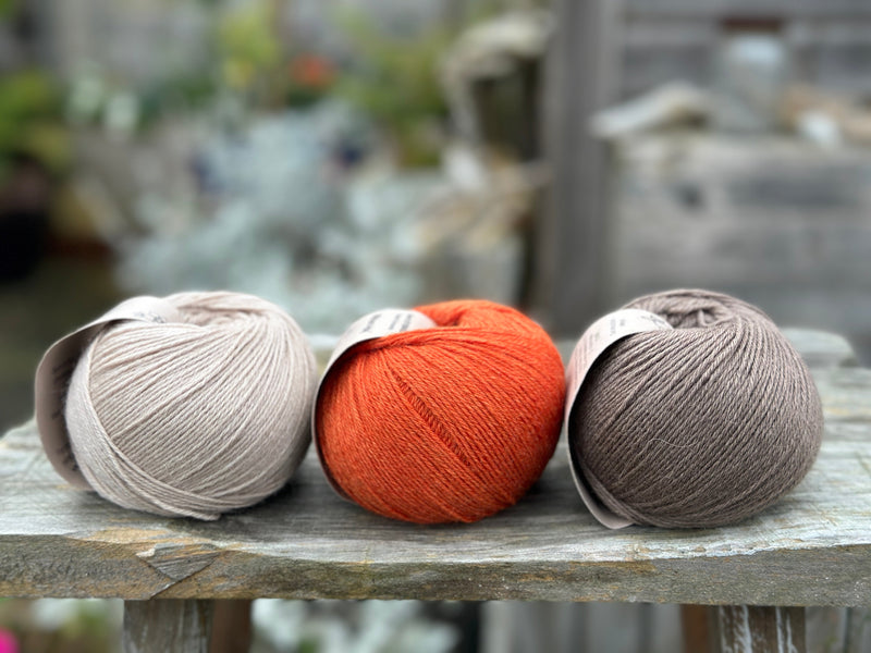 Three balls of yarn. From left to right: a beige ball, an orange ball and a brown ball