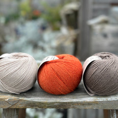 Three balls of yarn. From left to right: a beige ball, an orange ball and a brown ball