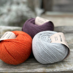 Three balls of yarn - one dark purple, one orange and one pale blue-grey