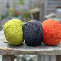 Three balls of yarn. From left to right - a green ball, a black ball and an orange ball