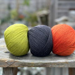 Three balls of yarn. From left to right - a green ball, a black ball and an orange ball