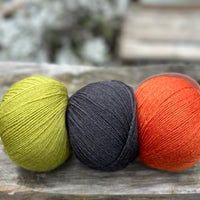 Three balls of yarn. From left to right - a green ball, a black ball and an orange ball