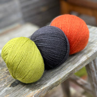 Three balls of yarn. From left to right - a green ball, a black ball and an orange ball